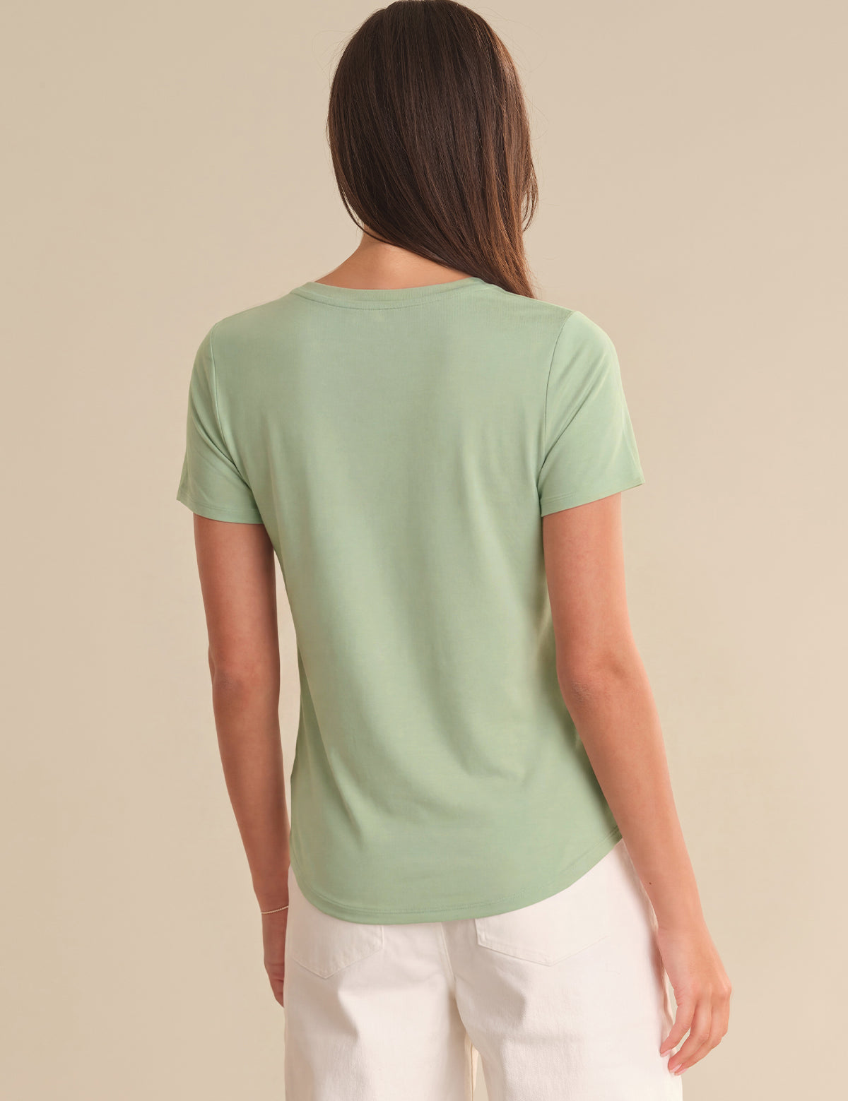 Woman wearing a light green t-shirt and white pants on a beige background