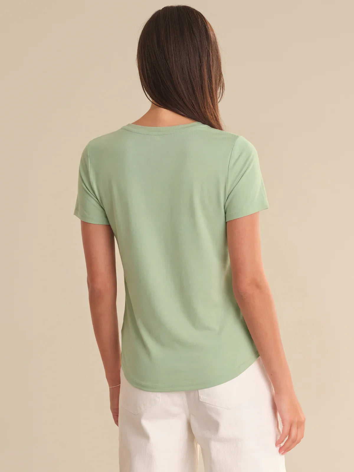 Woman wearing a light green t-shirt and white pants on a beige background