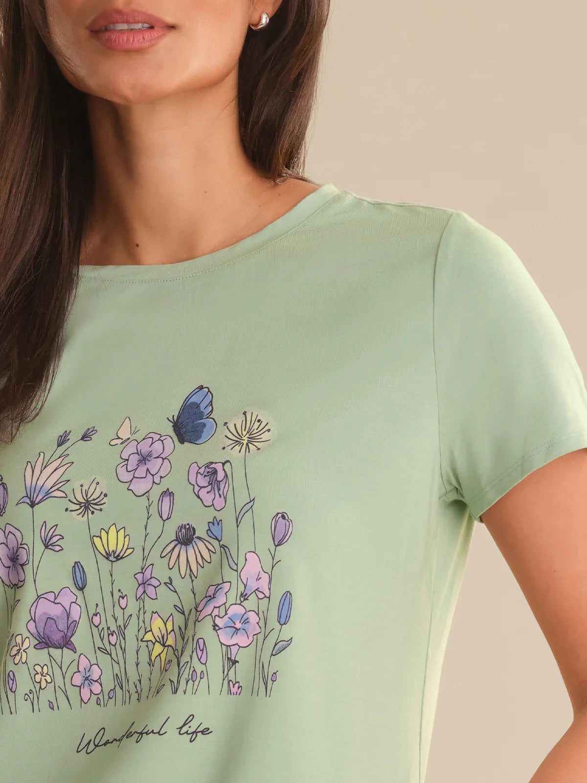 Woman wearing a light green t-shirt with floral designs and 'Happy Life' text.