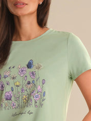 Woman wearing a light green t-shirt with floral designs and 'Happy Life' text.