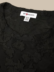 Close-up of a black textured lace top with a visible white neck label reading 89th Madison.