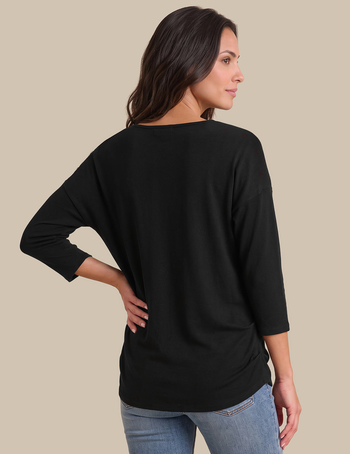 A woman shown from the back wearing a black three-quarter sleeve top and light blue jeans, standing against a solid beige background.