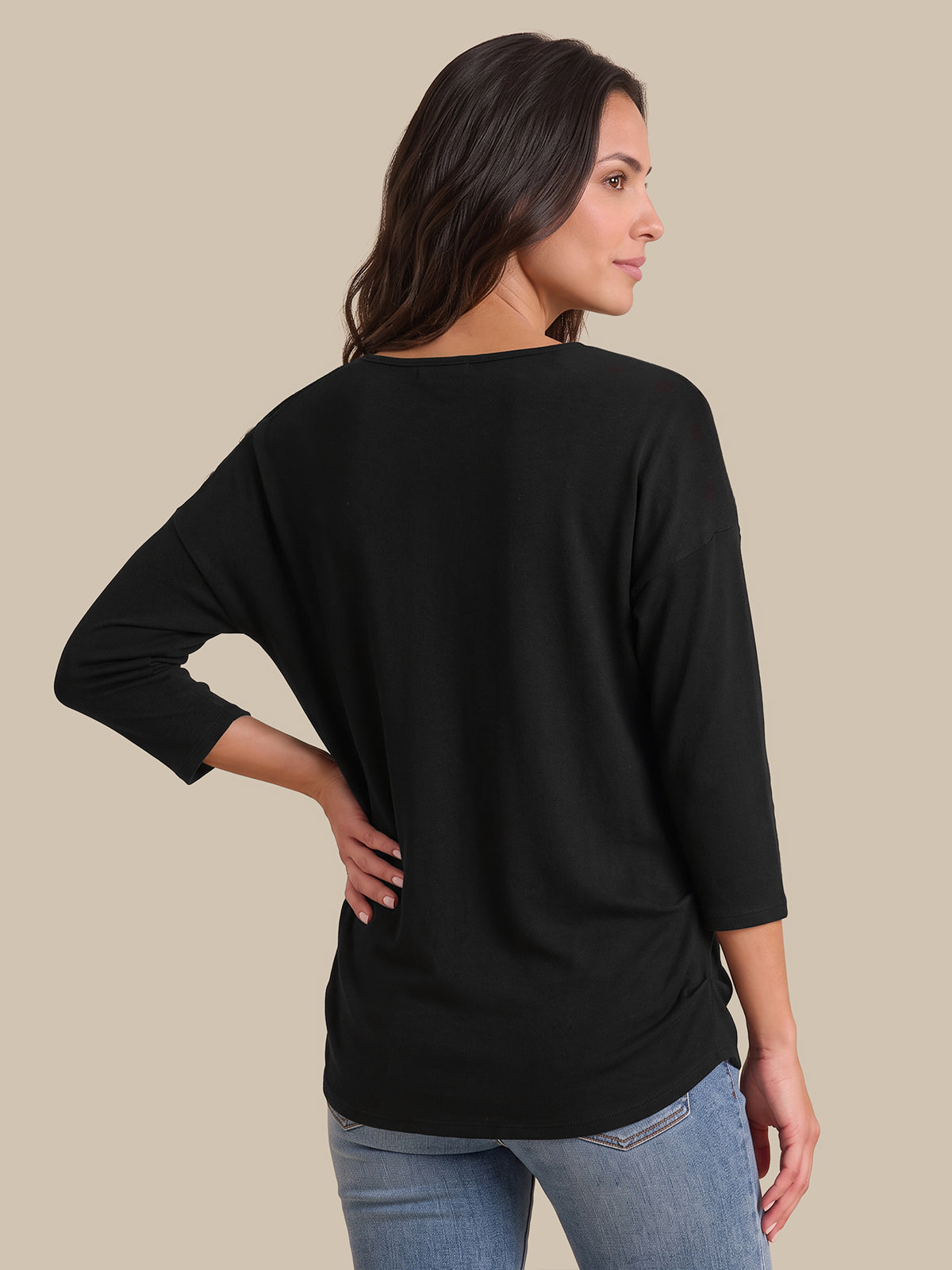 A woman shown from the back wearing a black three-quarter sleeve top and light blue jeans, standing against a solid beige background.