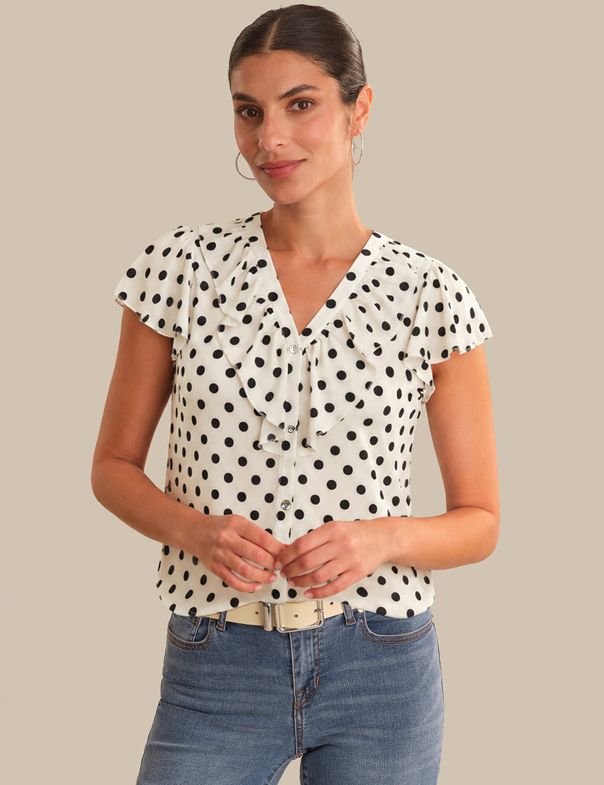 Woman wearing a polka dot blouse and jeans on a beige background