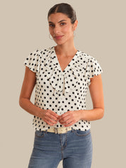 Woman wearing a polka dot blouse and jeans on a beige background