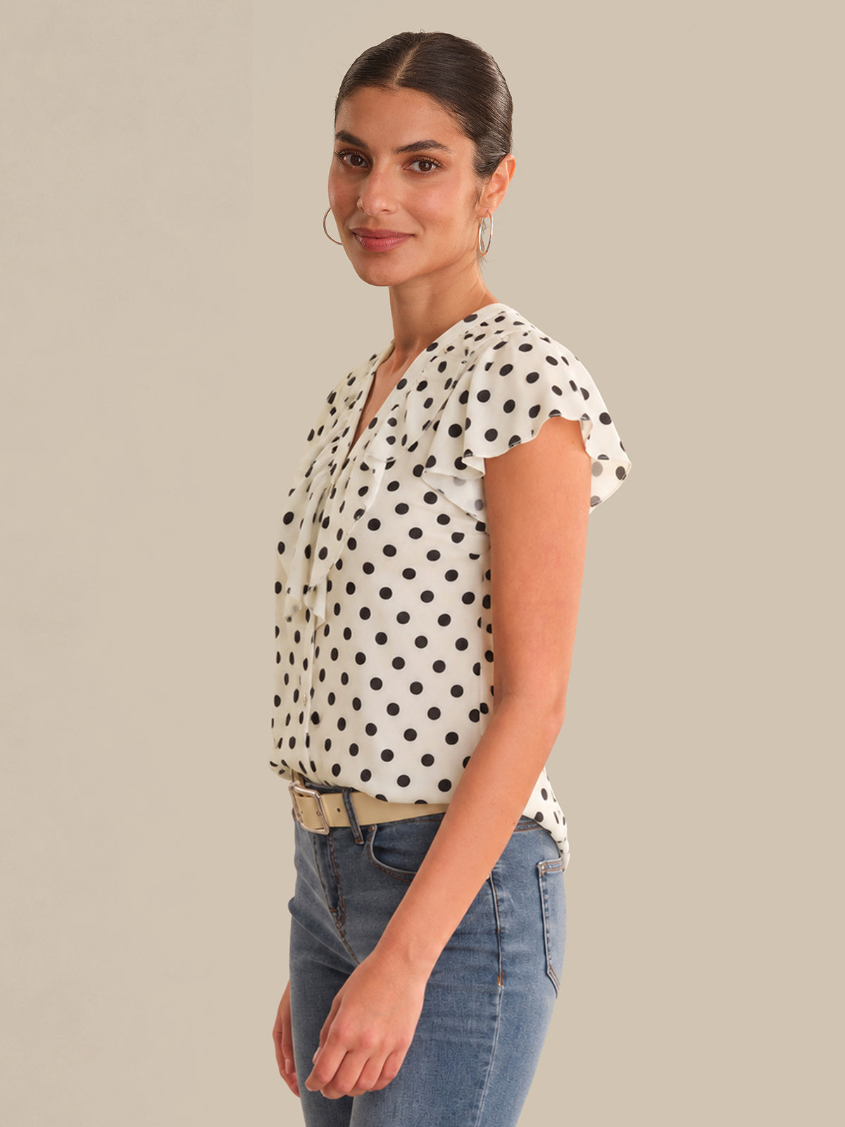 Woman wearing a polka dot blouse and jeans against a neutral background