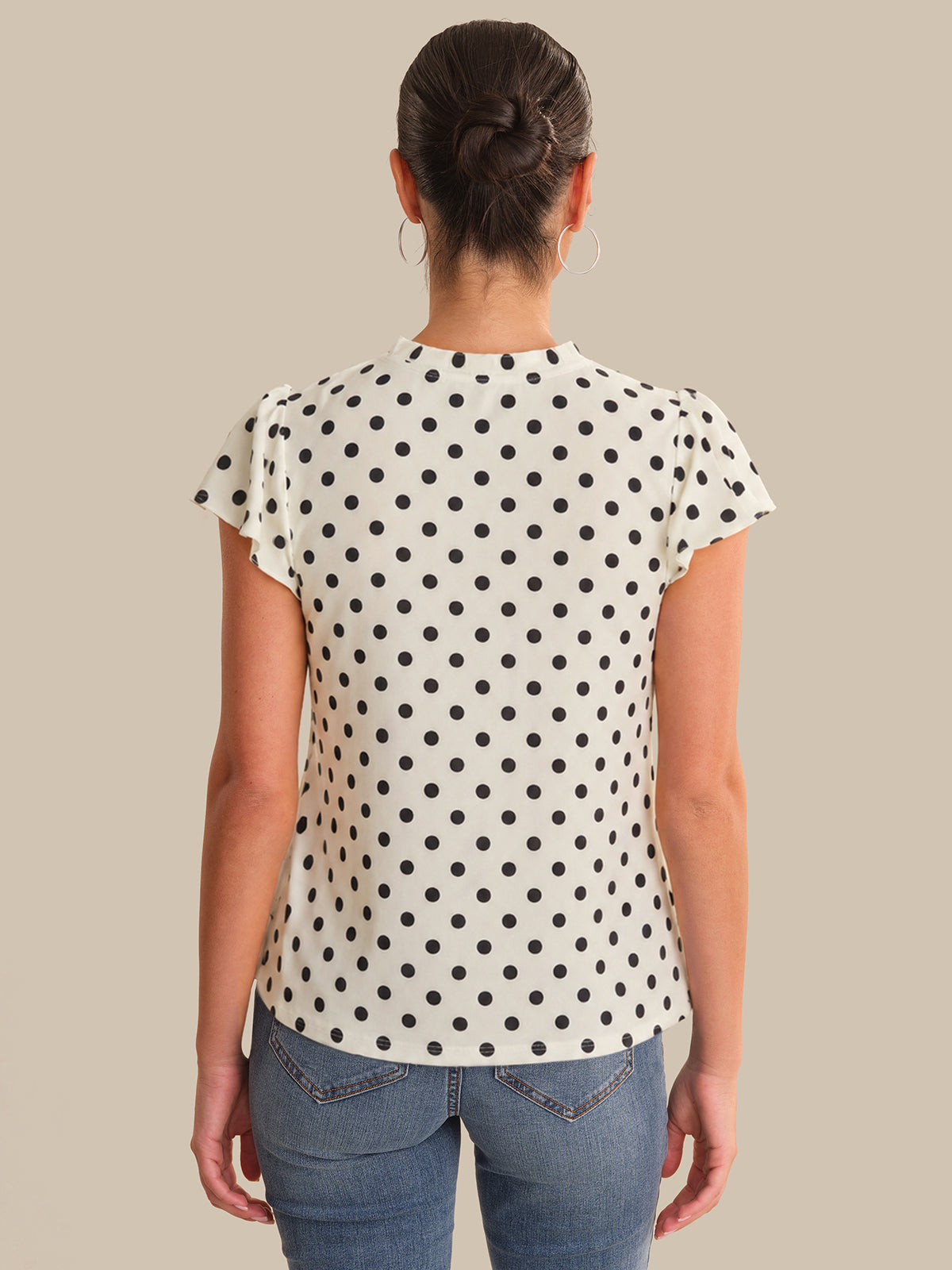 Person wearing a polka dot shirt and jeans on a beige background