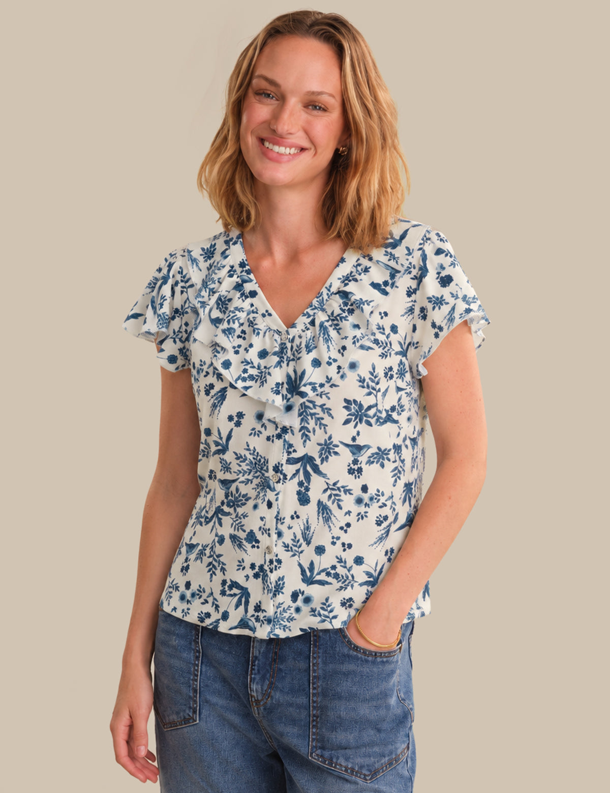 Woman wearing a blue floral blouse and jeans on a beige background