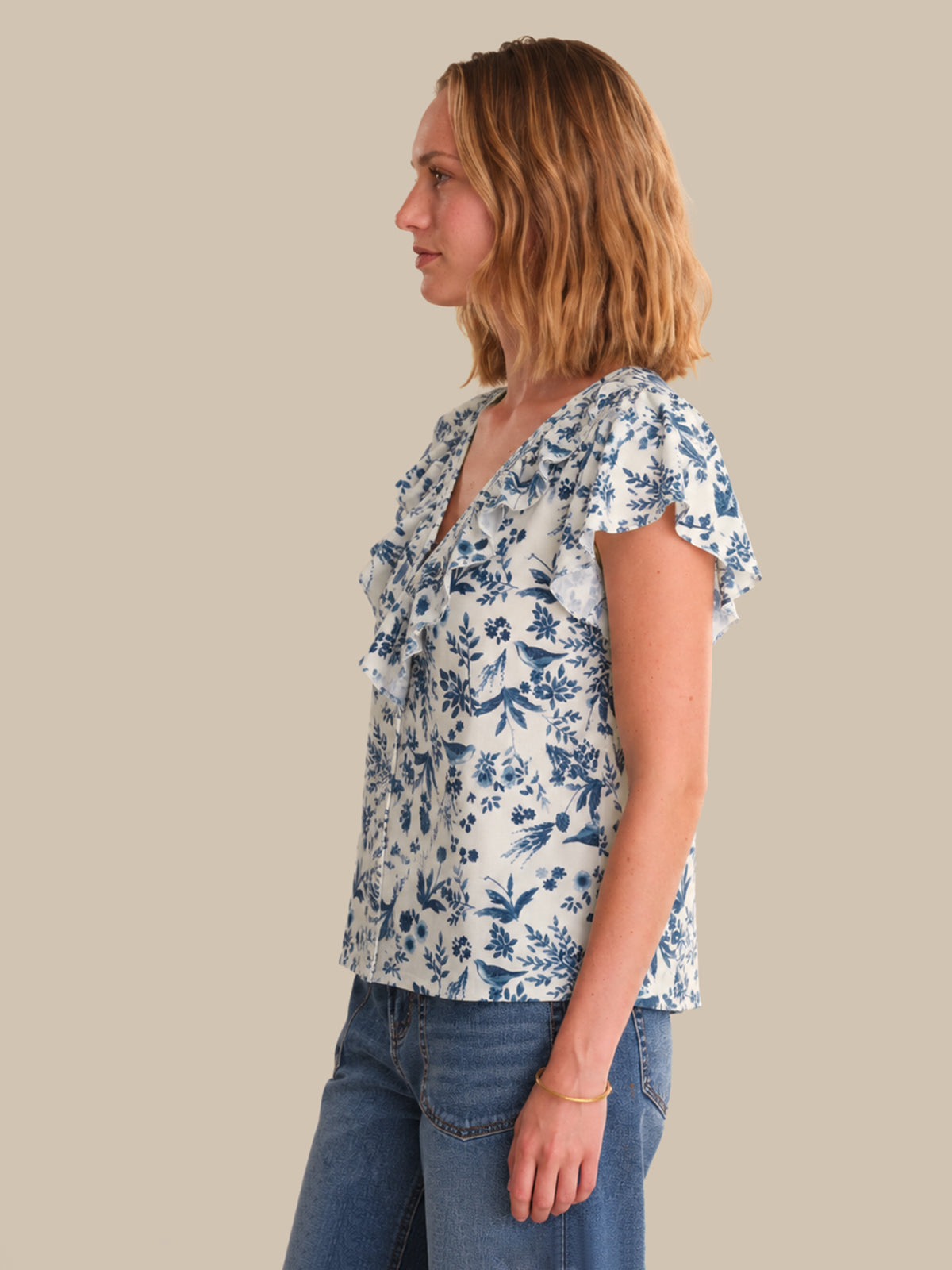 Woman wearing a floral blouse and jeans against a plain background