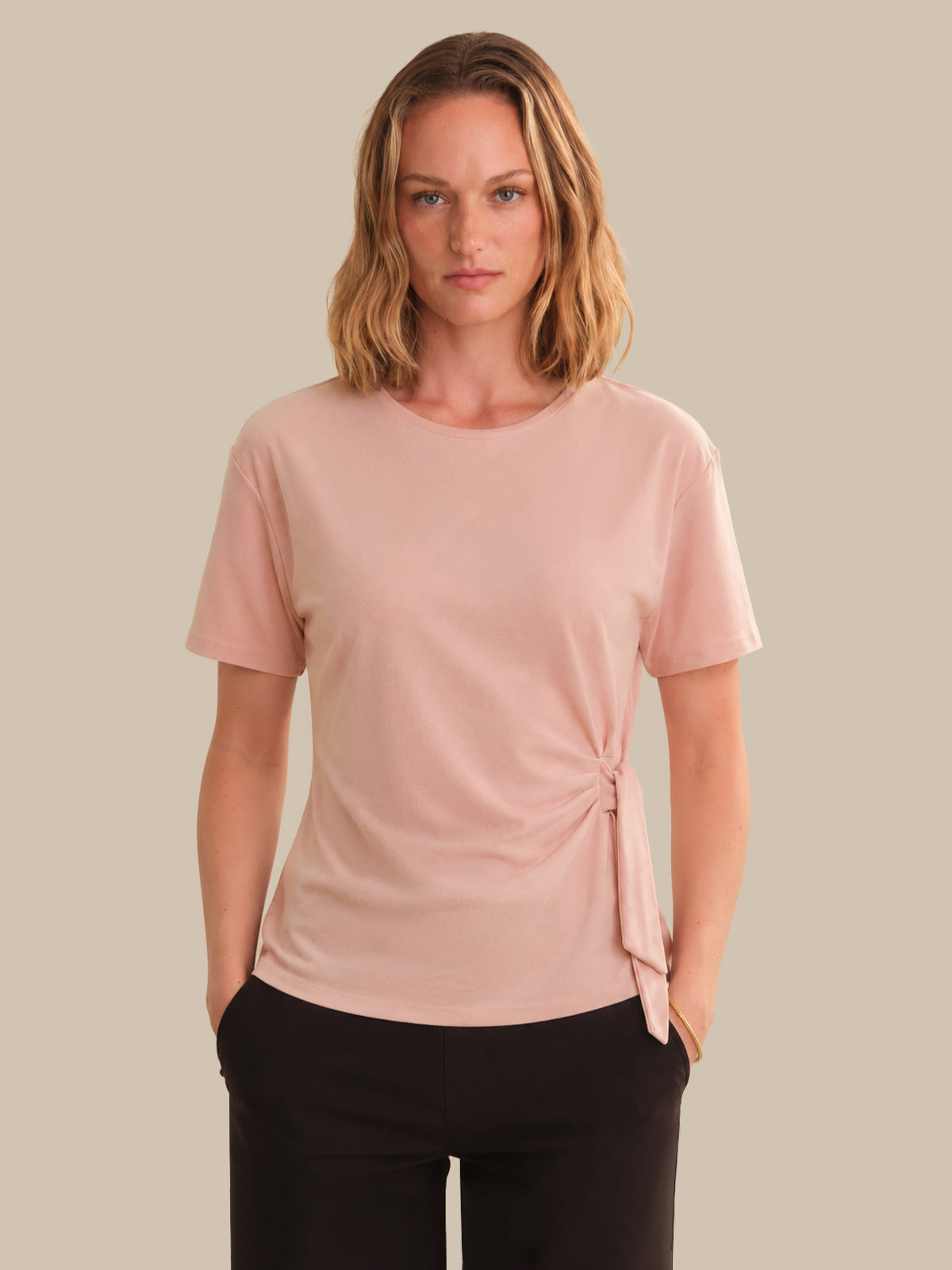 Woman wearing a pink t-shirt with a knot detail on a beige background