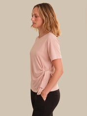 Woman wearing a light pink t-shirt with a knot detail on a plain background