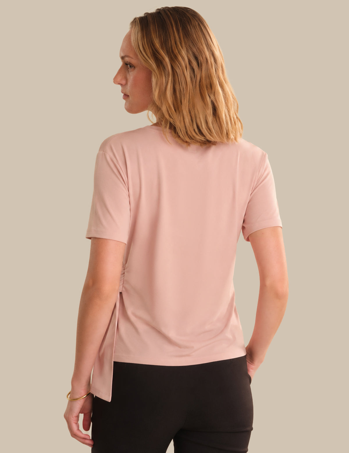 Woman wearing a pink t-shirt and black pants on a beige background
