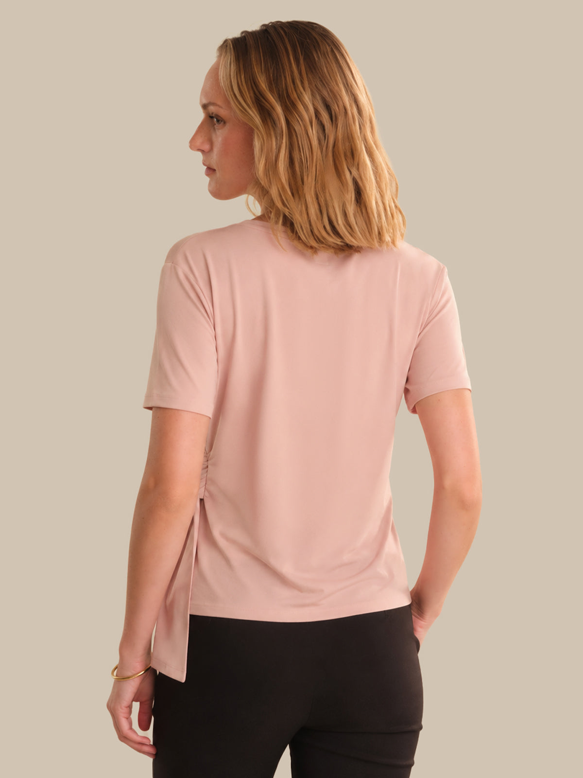 Woman wearing a pink t-shirt and black pants on a beige background