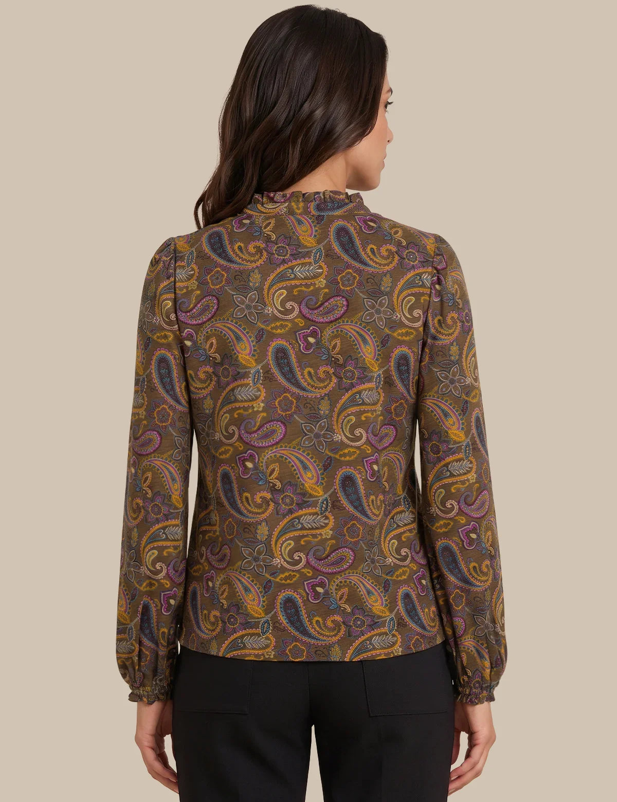 A woman shown from the back wearing a long-sleeve blouse with a brown paisley pattern in purple, gold, and orange, paired with black trousers, against a solid beige background.