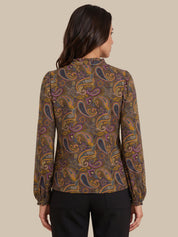 A woman shown from the back wearing a long-sleeve blouse with a brown paisley pattern in purple, gold, and orange, paired with black trousers, against a solid beige background.