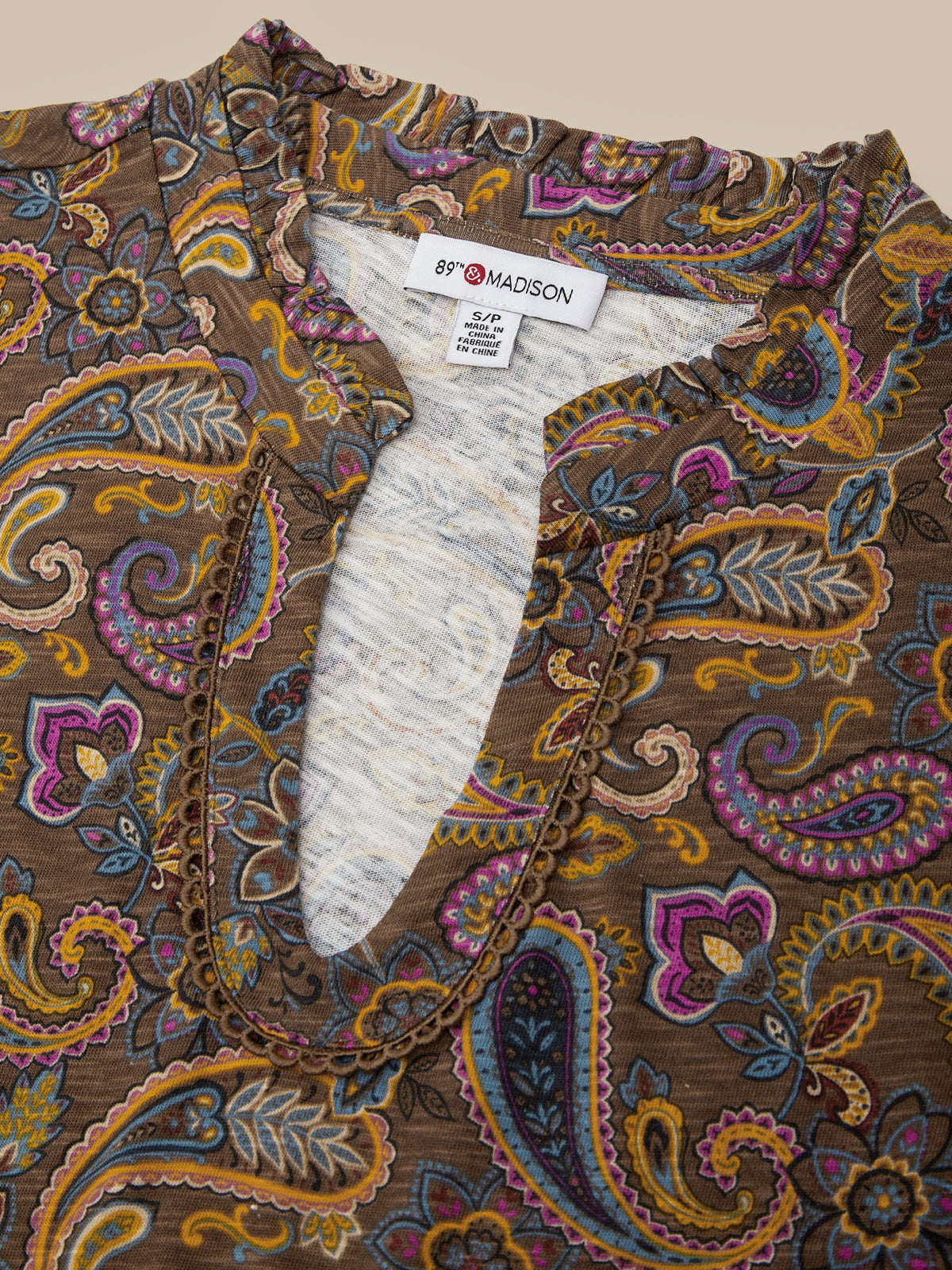 Close-up of a 89°Madson paisley blouse featuring a brown base with intricate multicolor paisley patterns in purple, yellow, blue, and orange, styled with a gold chain necklace.