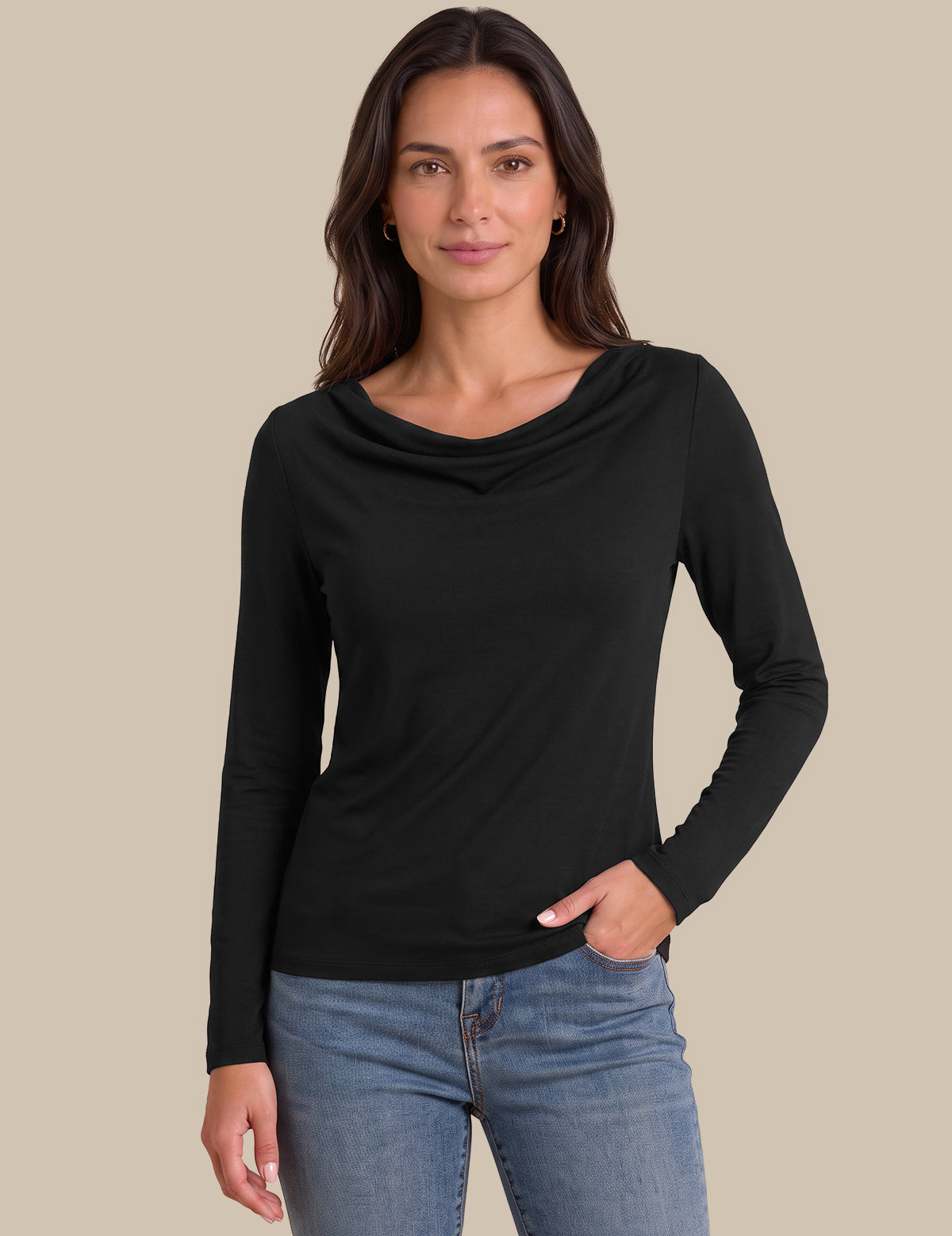 A woman modeling a black long-sleeve cowl neck top with blue jeans, set against a solid beige background.