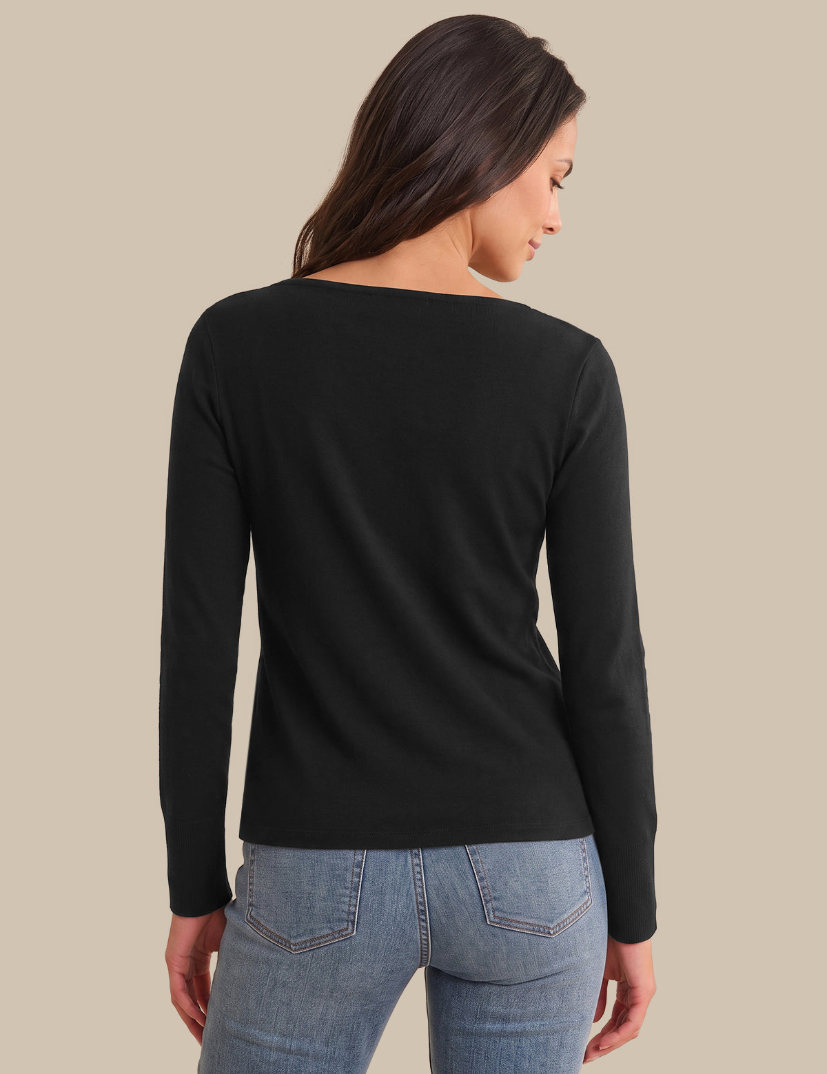 A woman shown from the back wearing a black long-sleeve boat-neck top and light blue jeans, set against a solid beige background.