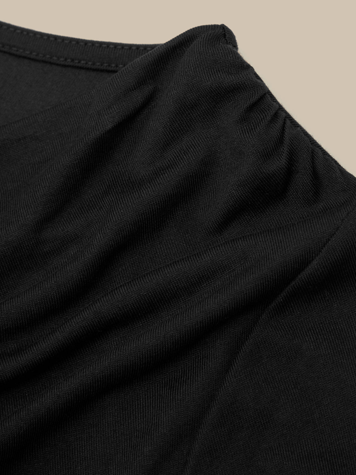 Close-up of a black ribbed knit garment, showing the texture and neckline detail against a light beige background.