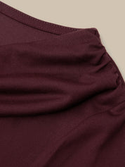 Close-up of a ribbed knit garment in deep burgundy, showing the fabric texture and a folded neckline against a light beige background.