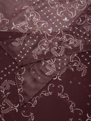 A close-up of a dark burgundy scarf with a white paisley and floral pattern, folded to show its texture and sheen.