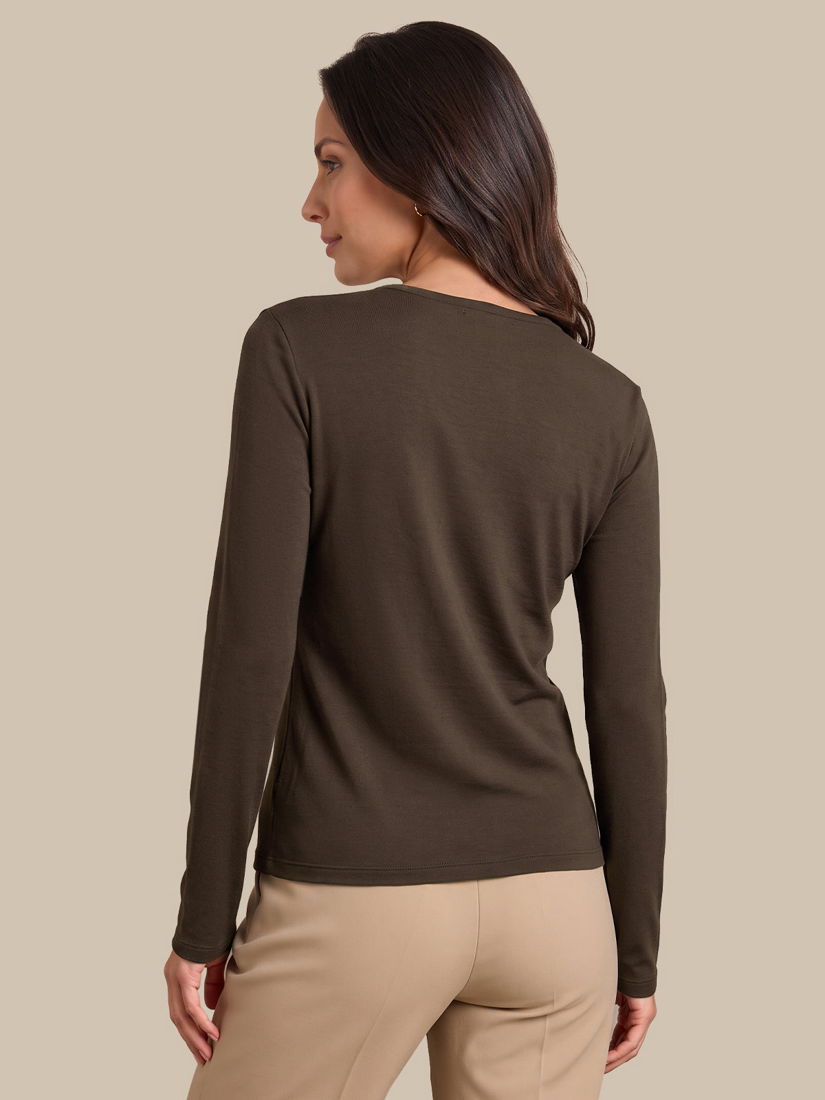 A woman shown from the back wearing a dark brown long-sleeve top and beige pants, photographed against a solid beige studio background.
