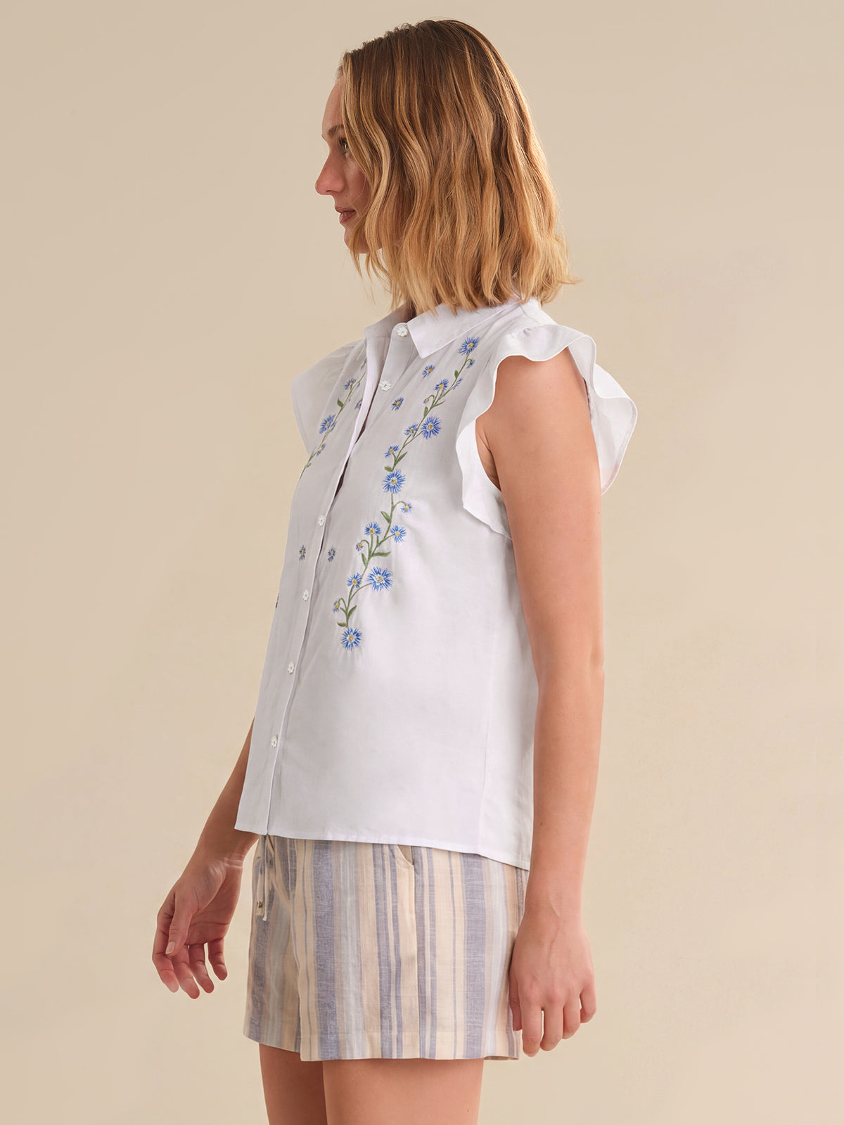 Woman wearing a white embroidered top and striped skirt on a beige background