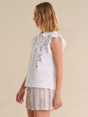 Woman wearing a white embroidered top and striped skirt on a beige background