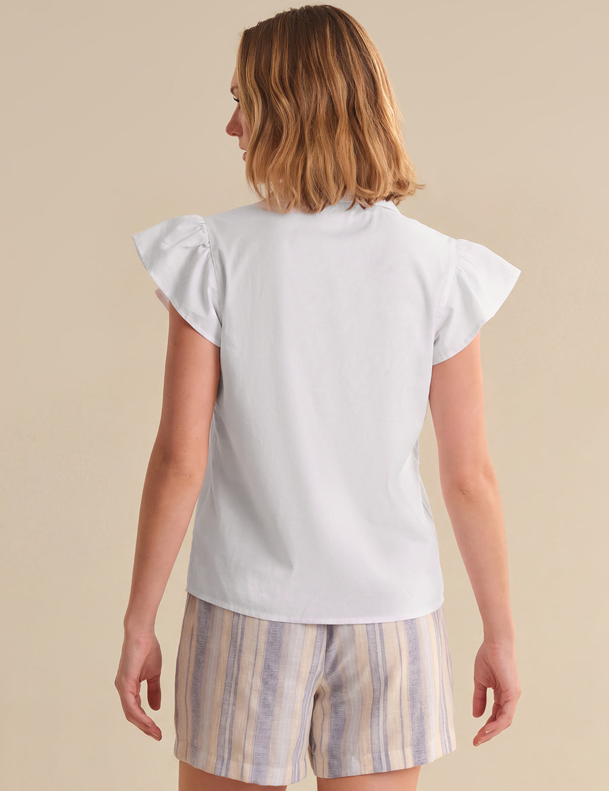 Woman wearing a white top and striped shorts on a beige background