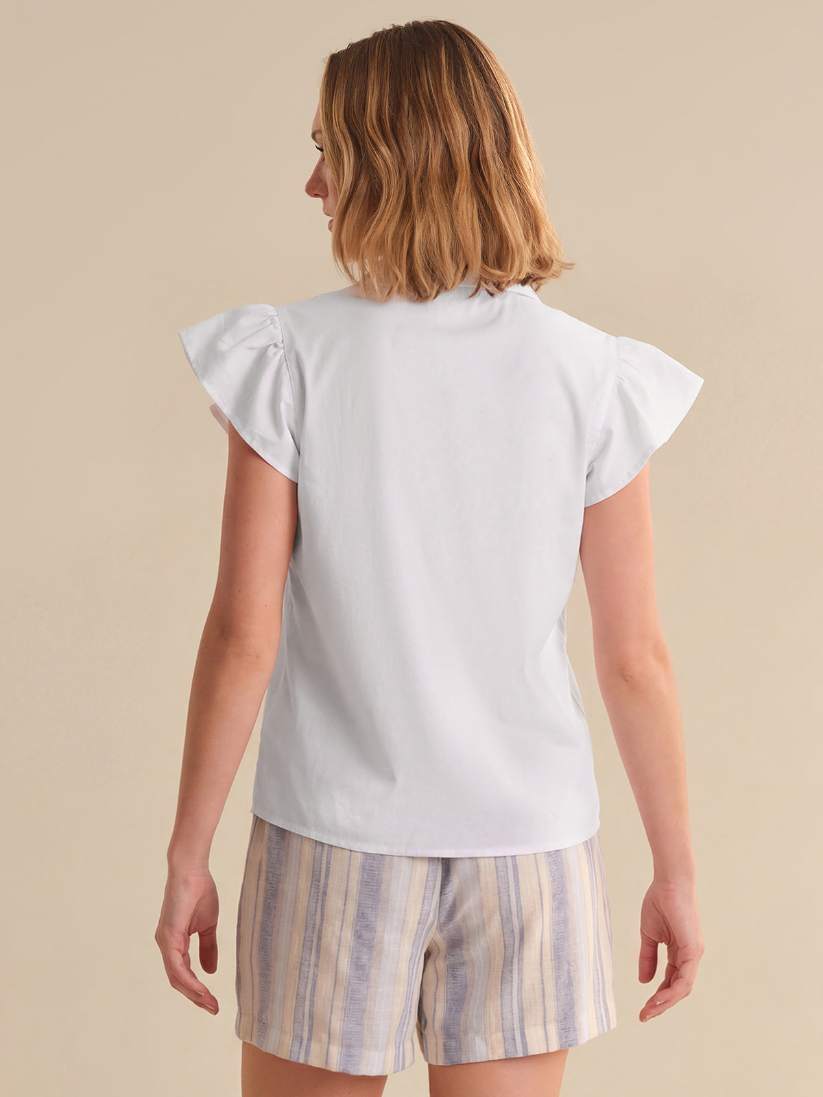Woman wearing a white top and striped shorts on a beige background