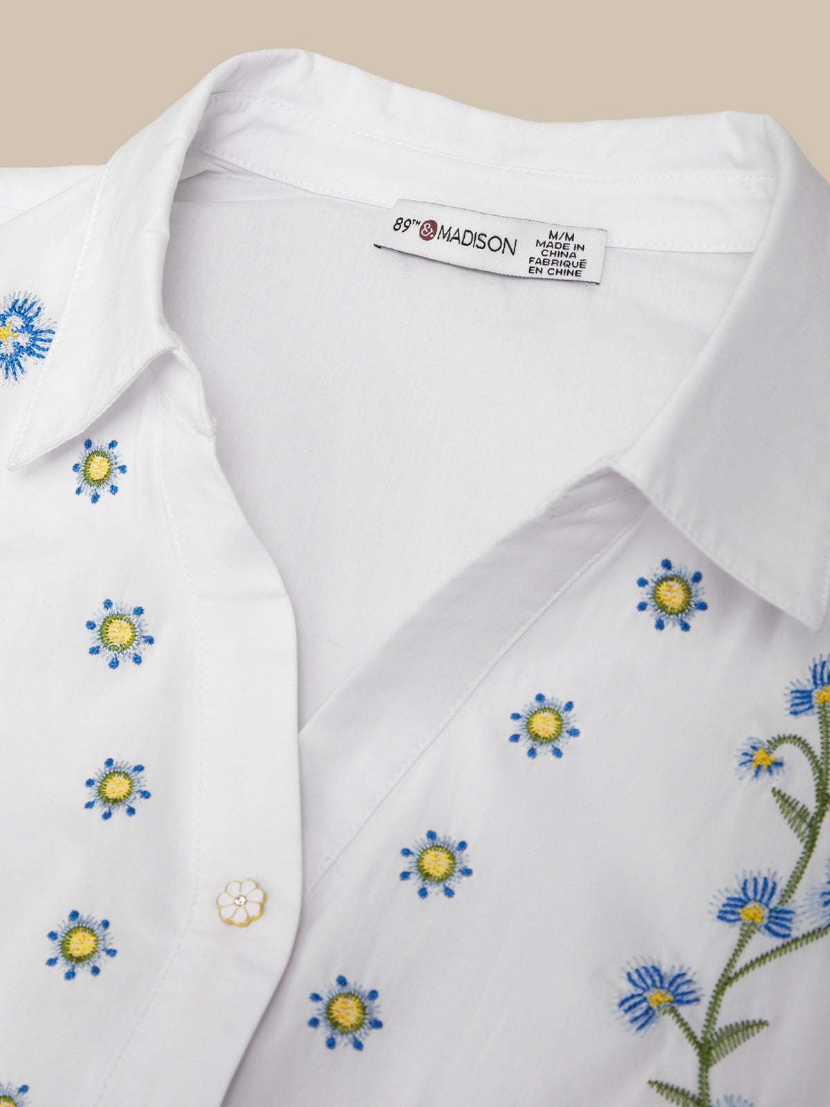 White dress shirt with floral embroidery and 'Madison' label on a beige background