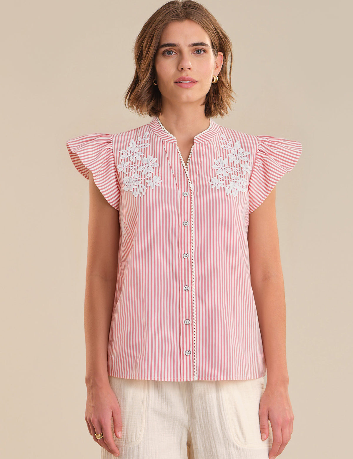 Woman wearing a red and white striped blouse with floral embroidery on a beige background