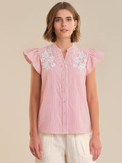 Woman wearing a red and white striped blouse with floral embroidery on a beige background