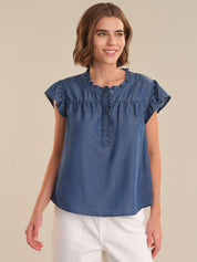Woman wearing a blue denim top with ruffled details on a beige background