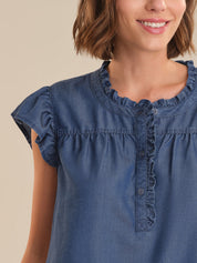 Woman wearing a blue denim dress with ruffled neckline on a beige background