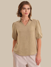 Woman wearing a beige blouse with puff sleeves against a beige background