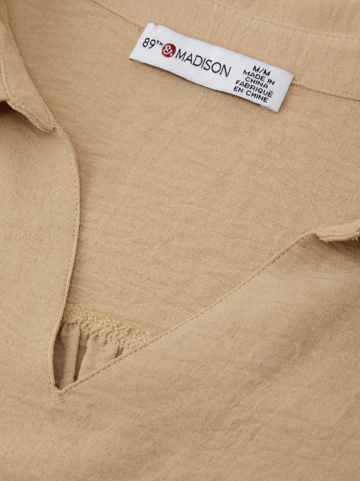 Close-up of a beige shirt with a 'Madison' label on a beige background