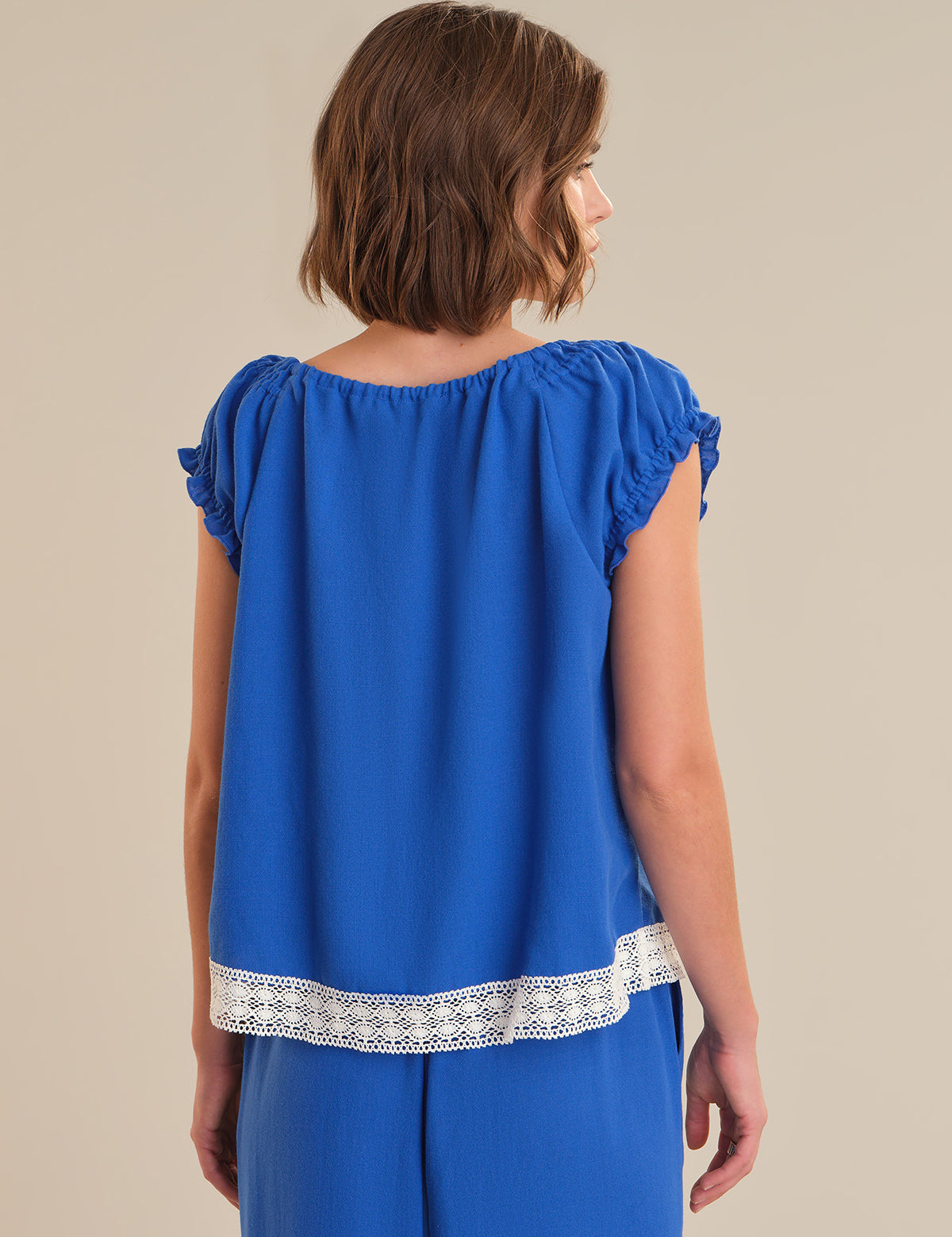 Woman wearing a blue top with lace trim on a beige background