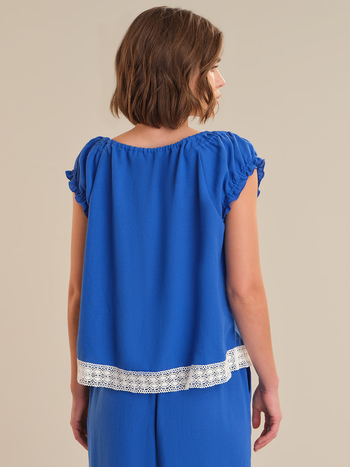 Woman wearing a blue top with lace trim on a beige background
