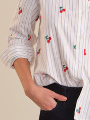 Close-up of a person wearing a white shirt with red cherry embroidery on a plain background