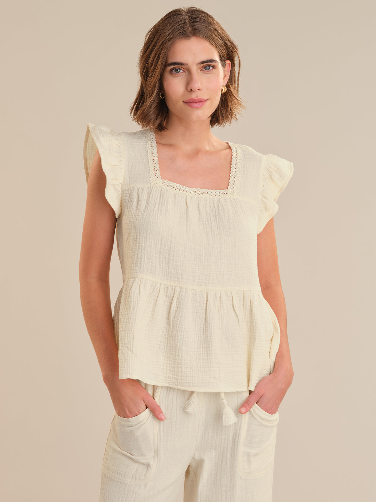 Woman wearing a light-colored top with ruffled sleeves against a neutral background