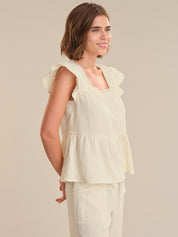 Woman wearing a light yellow sleeveless top with ruffled details on a beige background