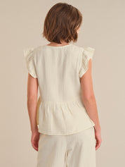 Woman wearing a white top with ruffled sleeves on a beige background