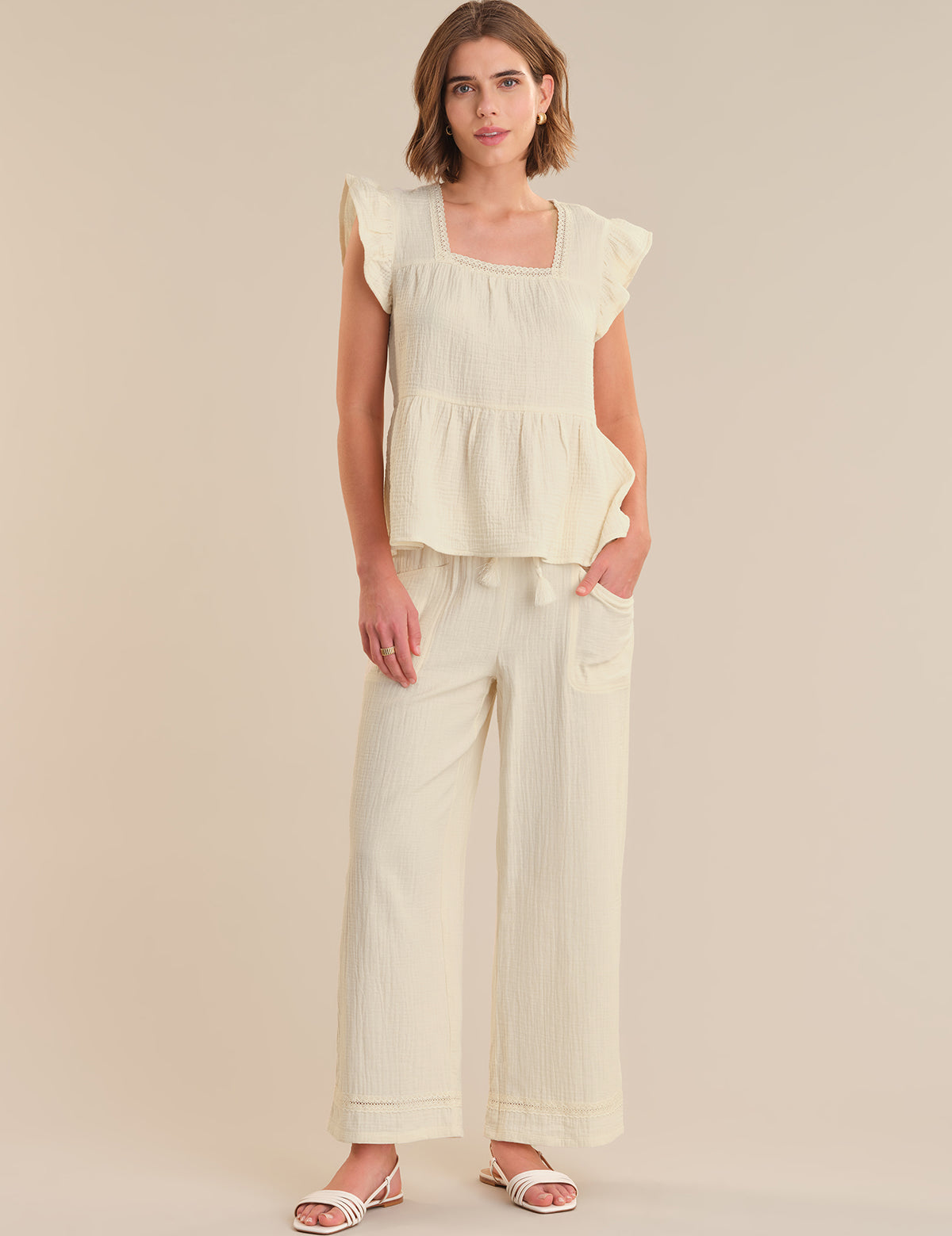 Woman wearing a light-colored top and wide-leg pants on a plain background