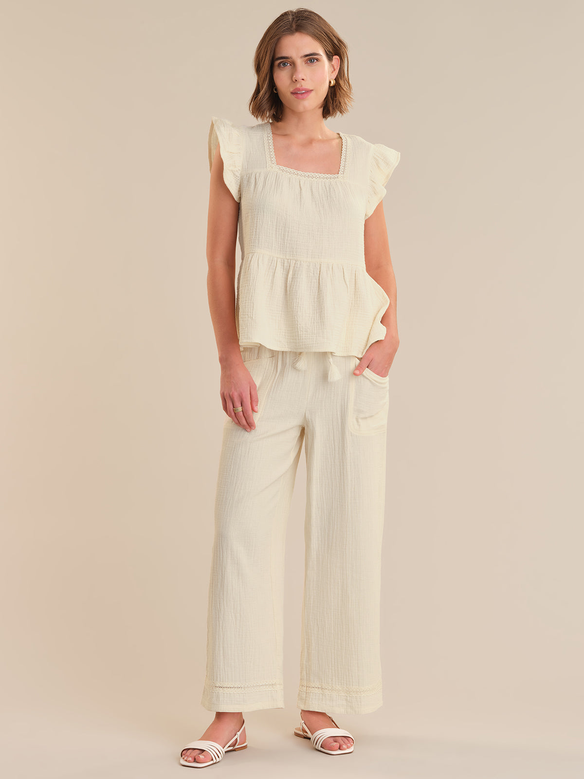 Woman wearing a light-colored top and wide-leg pants on a plain background