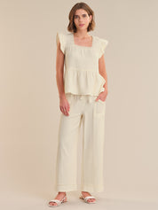 Woman wearing a light-colored top and wide-leg pants on a plain background