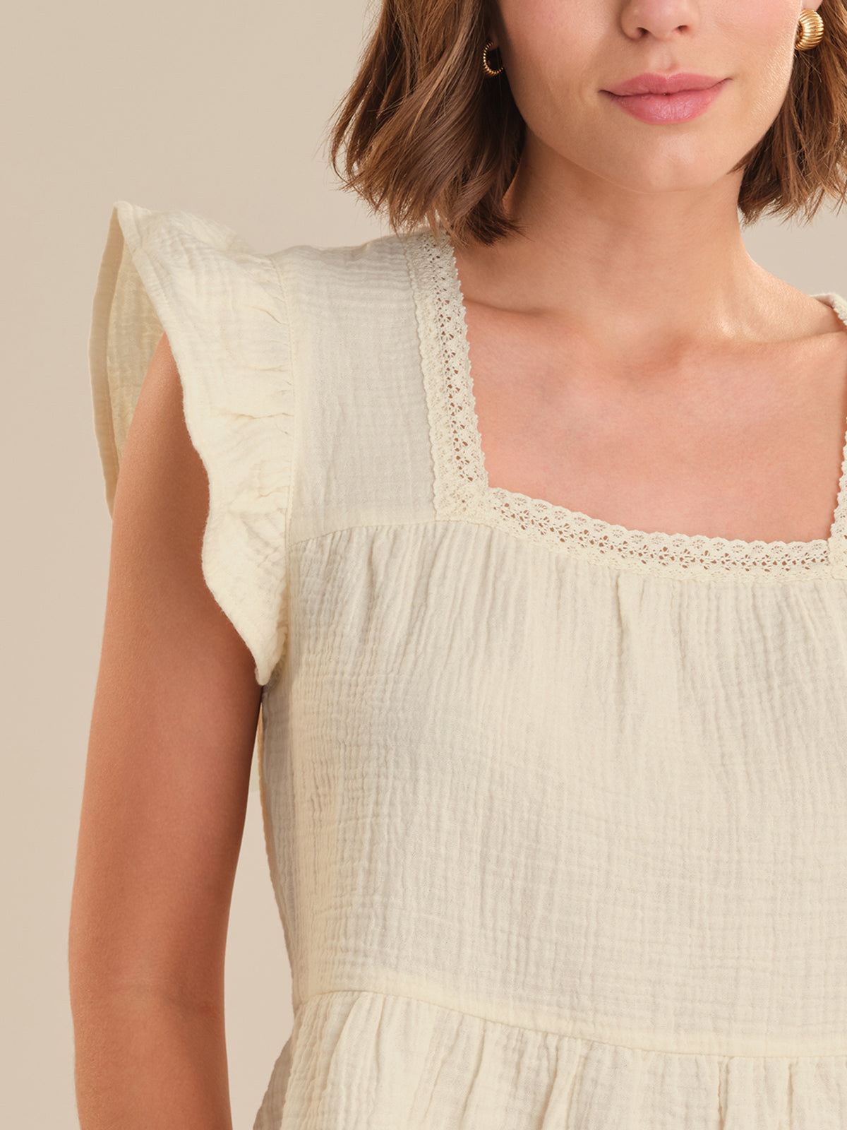Close-up of a person wearing a light-colored top with lace details on a neutral background