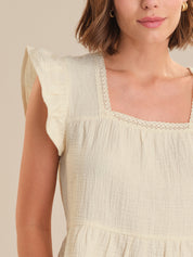 Close-up of a person wearing a light-colored top with lace details on a neutral background