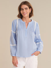 Woman wearing a light blue striped blouse with white trim on a beige background
