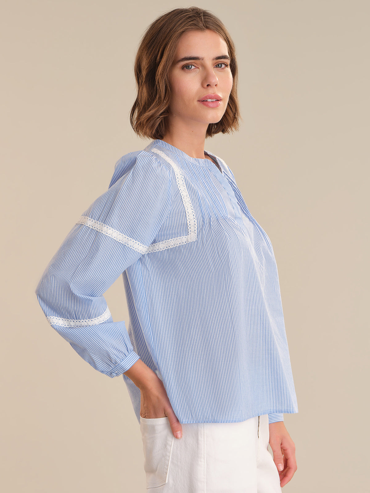 Woman wearing a light blue striped blouse with white trim on a beige background